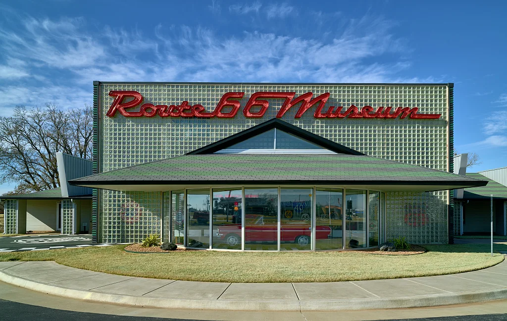 The Oklahoma Route 66 Museum in Clinton, with its red script sign and a vintage car visible behind the front glass.
